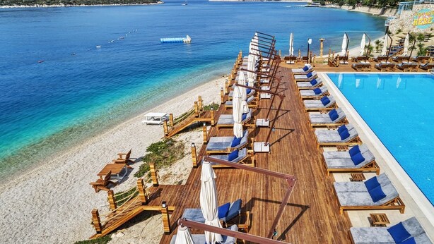 A wooden deck with lounge chairs and umbrellas overlooking a clear blue sea and a swimming pool. - Doria Hotel&Yacht Club (Kaş)