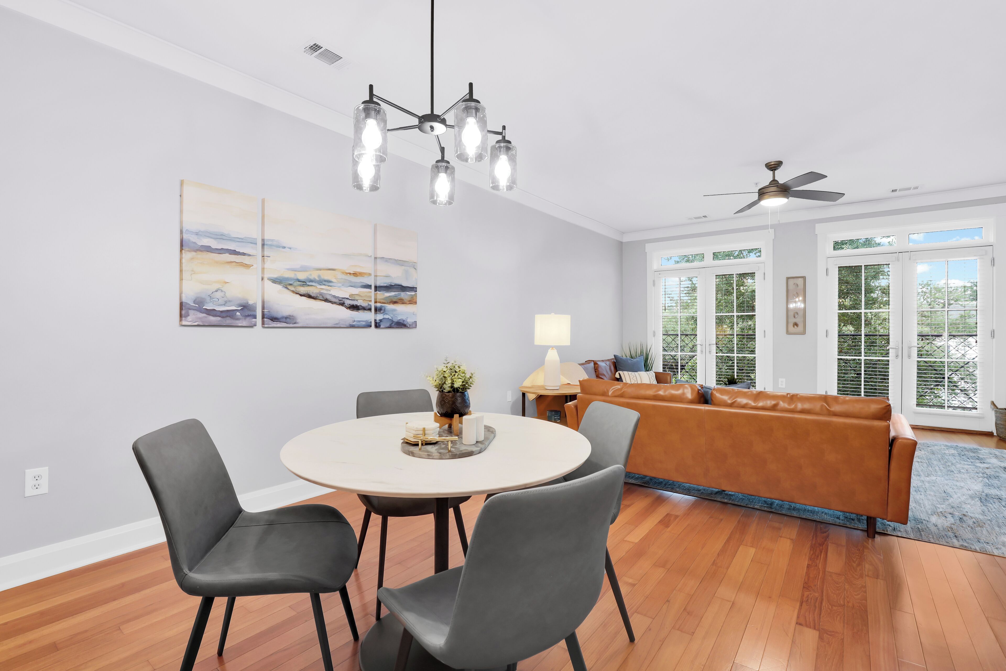 A modern dining area with a round table, two chairs, a chandelier, and artwork on the wall.
