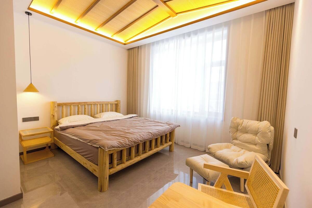 A bedroom with a wooden bed, a bedside table, a chair, and a window with curtains.
