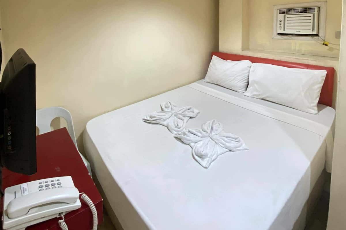 Una habitación de hotel con una cama, un escritorio con teléfono y un aire acondicionado instalado en la pared.