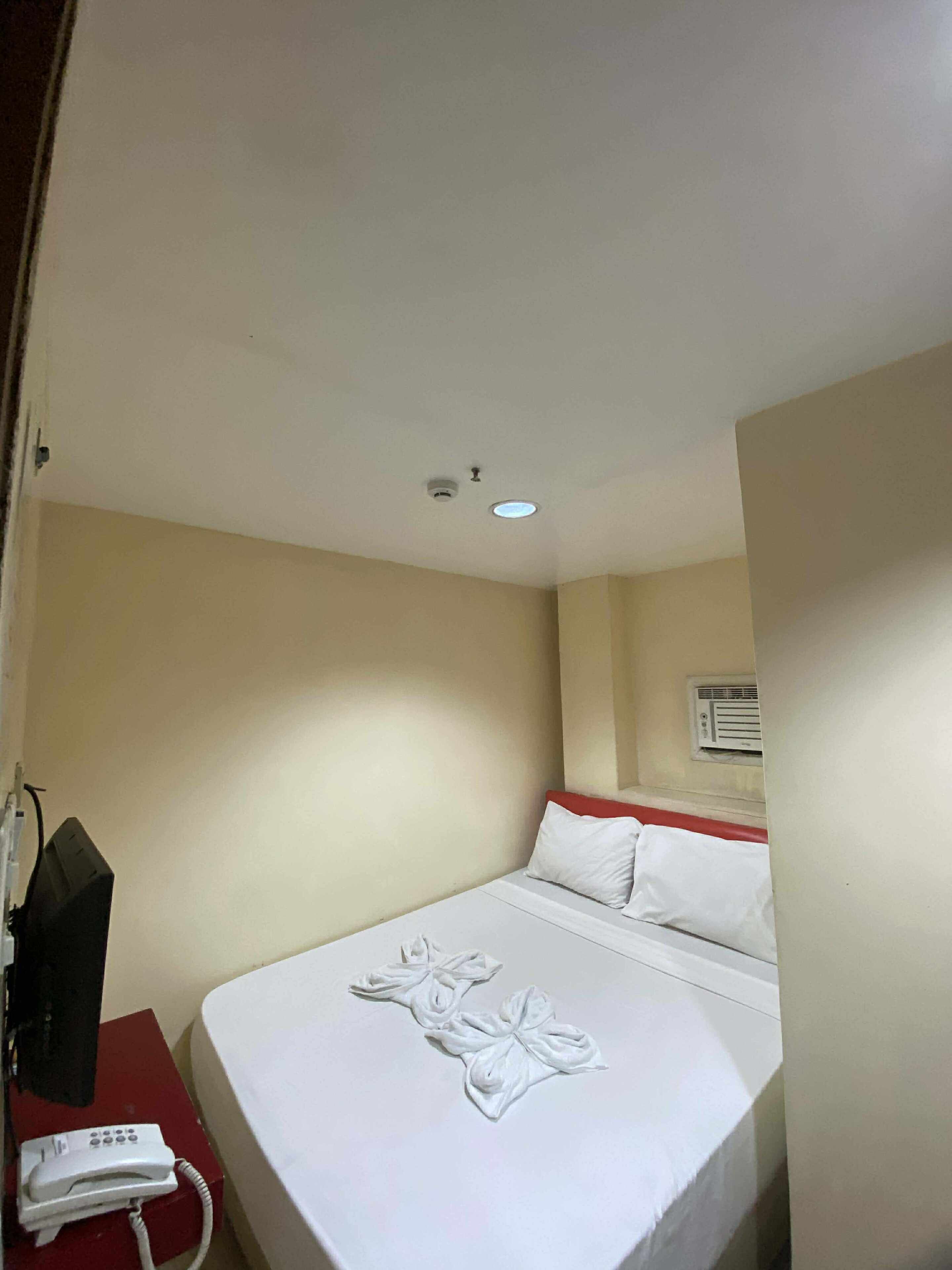 Una habitación de hotel con una cama, un escritorio con teléfono y una lámpara en el techo.