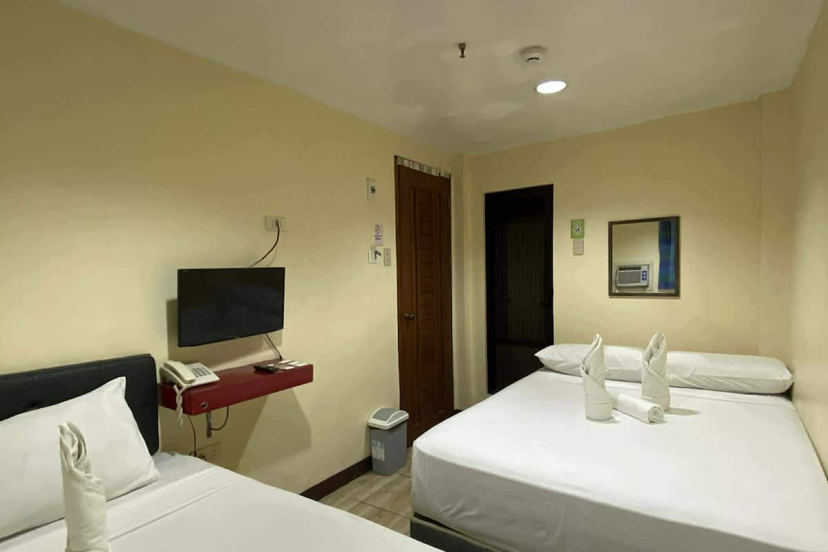 Habitación de hotel con dos camas, un escritorio con teléfono, un cesto de basura y un televisor montado en la pared.