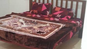 A bed with a patterned bedspread and pillows, a wooden headboard, and a visible electrical outlet on the wall.