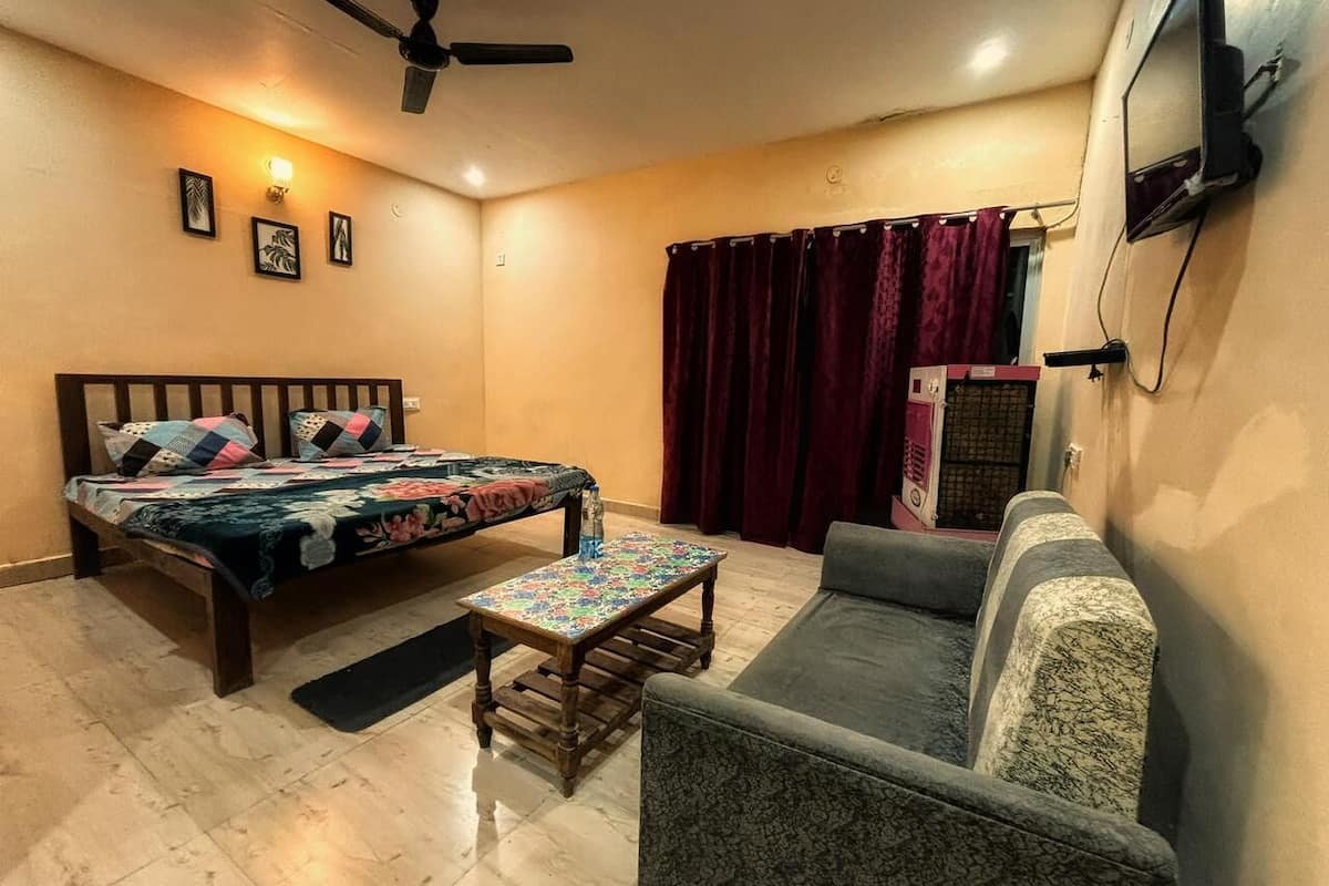 Una habitación con cama, sofá, una mesita, ventilador de techo y televisor en la pared.
