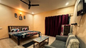 Un dormitorio con cama, sofá, una mesita, ventilador de techo y televisor montado en la pared.