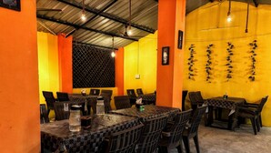 Un restaurante con mesas y sillas altas, un ventilador de techo y una pared amarilla con detalles decorativos.