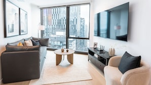 A modern living room with a sofa, armchair, and coffee table, large windows with a city view, and a flat-screen TV mounted on the wall. - The Queensbridge Skyline Suite, Heated Pool, Gym, Sauna, Steam next to Casino (Southbank)