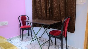 Una habitación con cama, una mesita, dos sillas y un ventanal con cortinas.