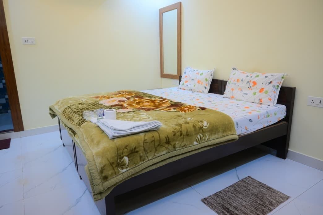 A neatly made bed with a floral bedspread and pillows, a bedside table with a folded towel, and a small rug on the floor.