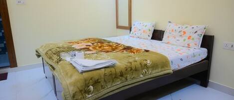 A neatly made bed with a floral bedspread and pillows, a bedside table with a folded towel, and a small rug on the floor.