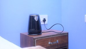 Una tetera negra sobre un mueble de madera con un enchufe en una habitación con paredes azules.