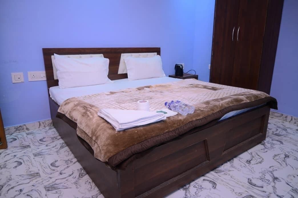 Un lit bien fait, avec une couverture marron et des oreillers blancs, une table de chevet avec une bouilloire et une armoire dans une pièce dont le sol est recouvert de carreaux décoratifs.