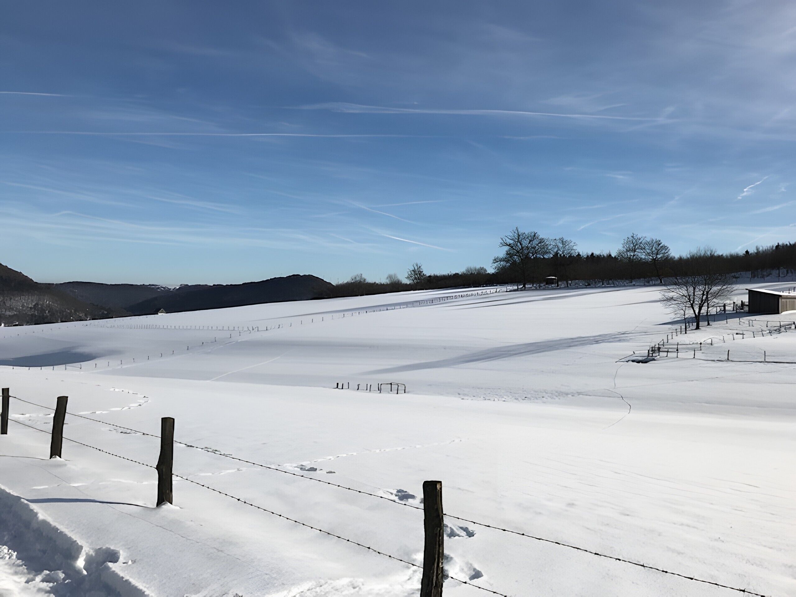 A snow-covered field with a fence, a building, and a clear sky.