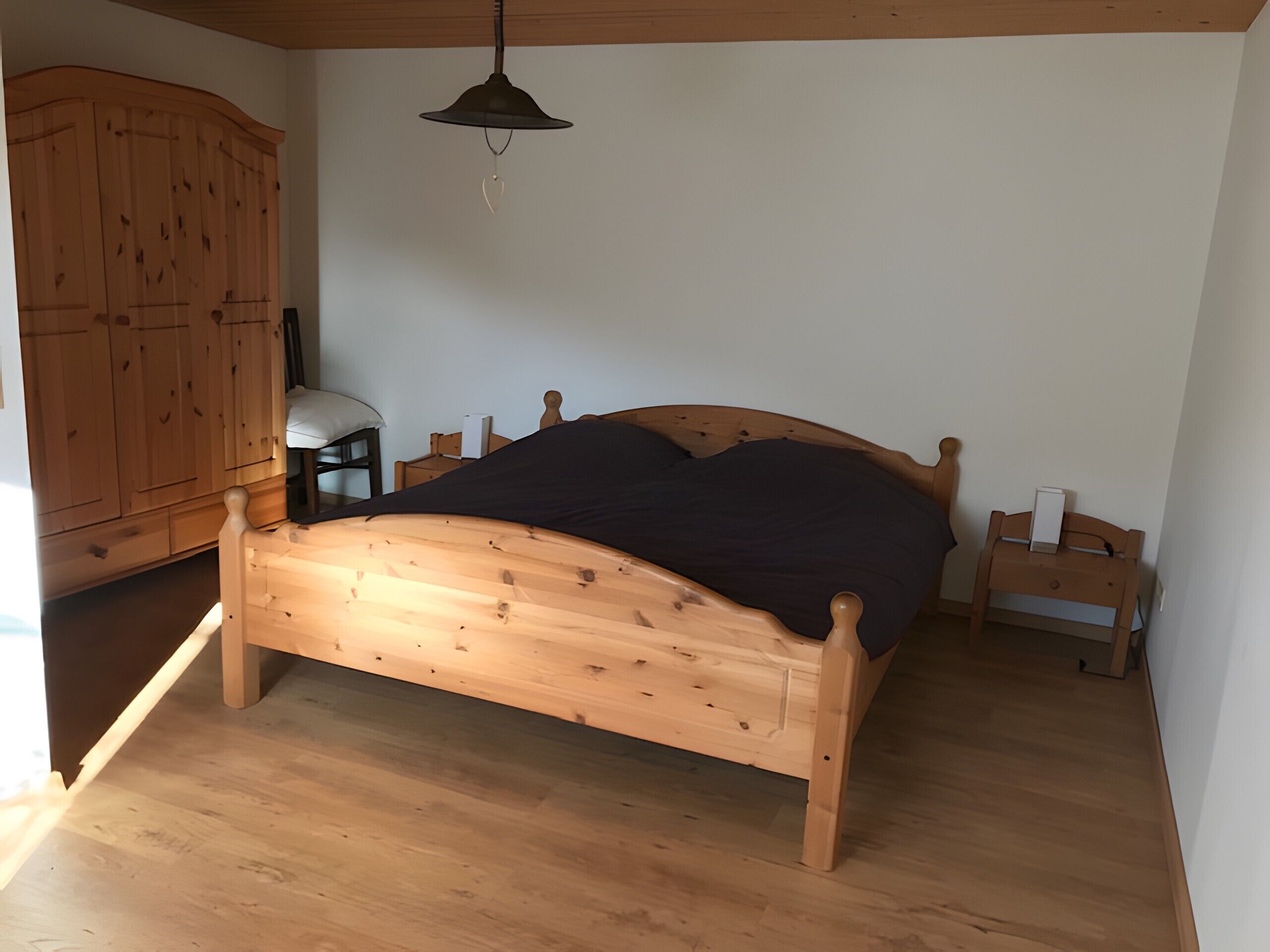 A wooden bed with a headboard, a wooden wardrobe, and a bedside table with a lamp.