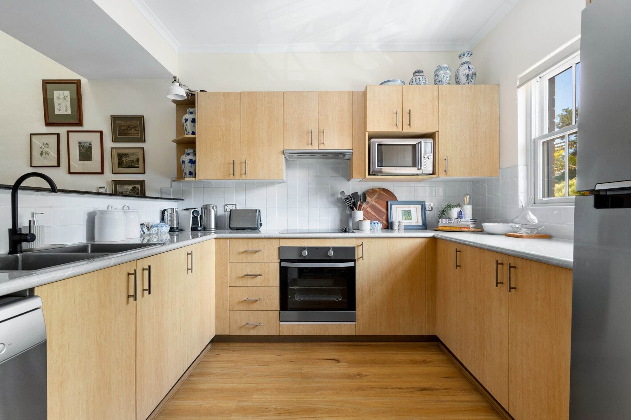 A modern kitchen with wooden cabinets, a built-in oven, a microwave, and a window providing natural light.