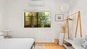 A modern bedroom with a large window, a bed, a bedside table, a chair, and a small desk with a lamp. - Spacious 2-Bed Townhouse with a Lush Courtyard (Erskineville)