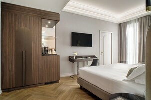 A hotel room with a large bed, a desk with a chair, a TV mounted on the wall, and a wardrobe.