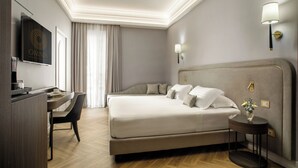 A hotel room with a large bed, a desk with a chair, a TV, and a wall-mounted lamp. - Aria Palace by OMNIA Hotels (Rome)