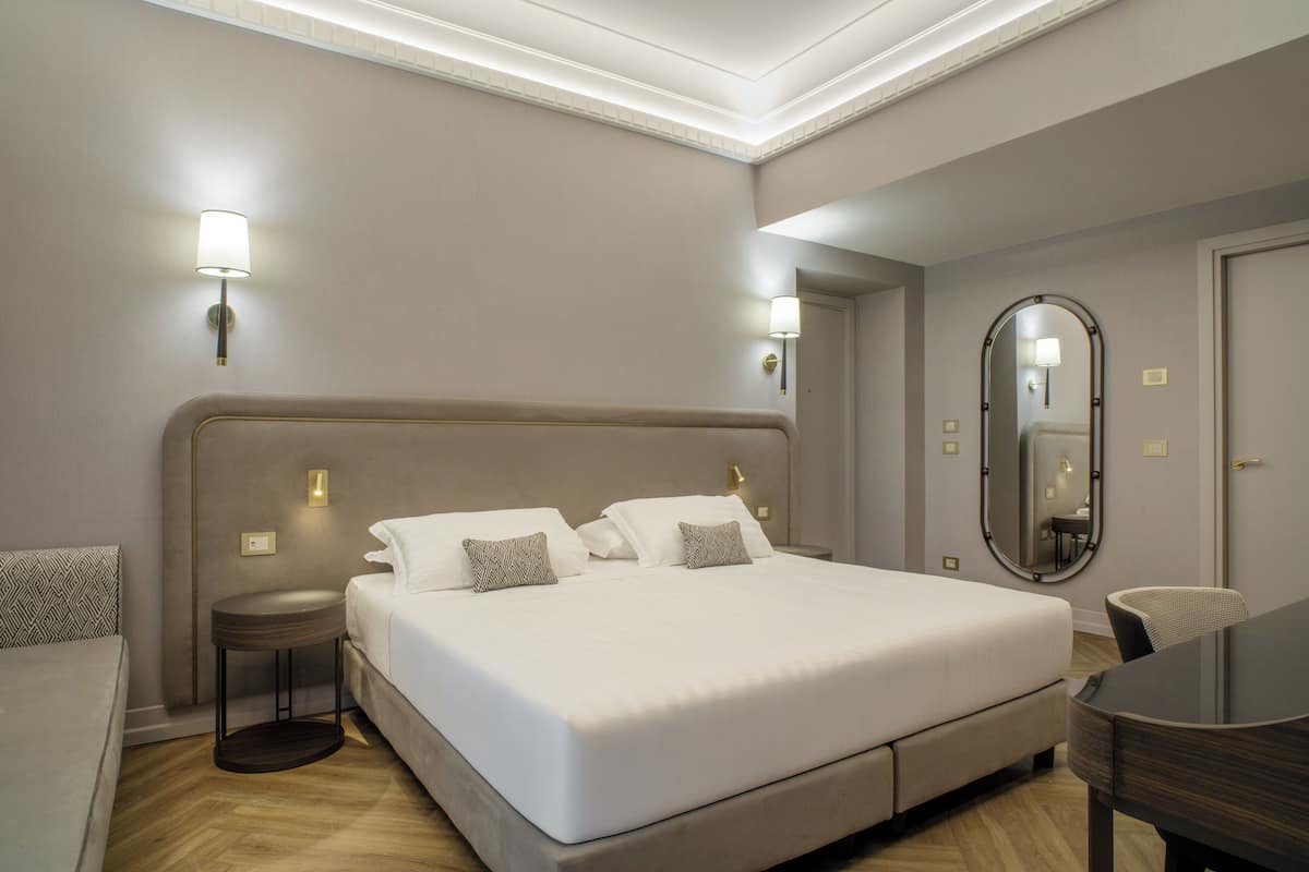 Une chambre d’hôtel moderne avec un grand lit, des tables de chevet, un miroir rond et une petite table.