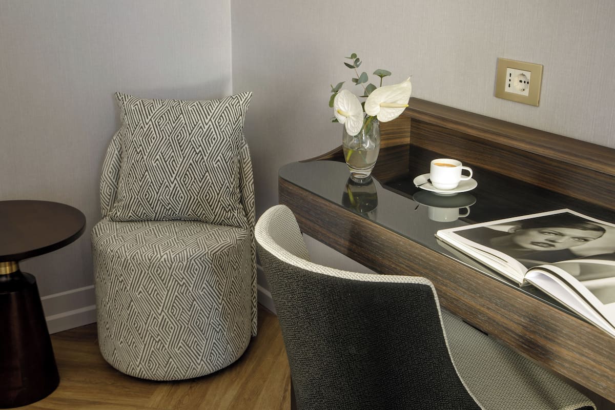 Une chambre moderne avec un fauteuil à motifs, une petite table sur laquelle se trouve un vase de fleurs, une tasse et un magazine.