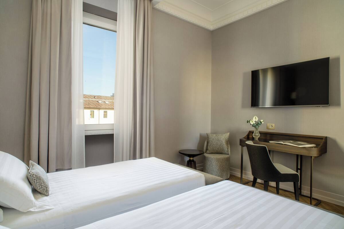 Une chambre d’hôtel avec deux lits, un bureau, une chaise, une télévision et une fenêtre avec des rideaux.