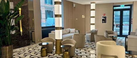 A lobby with a marble floor, a sofa, armchairs, and a potted plant.