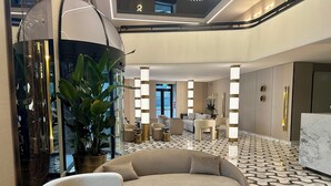 A modern lobby with a curved sofa, round tables, and a large potted plant. - Aria Palace by OMNIA Hotels (Rome)