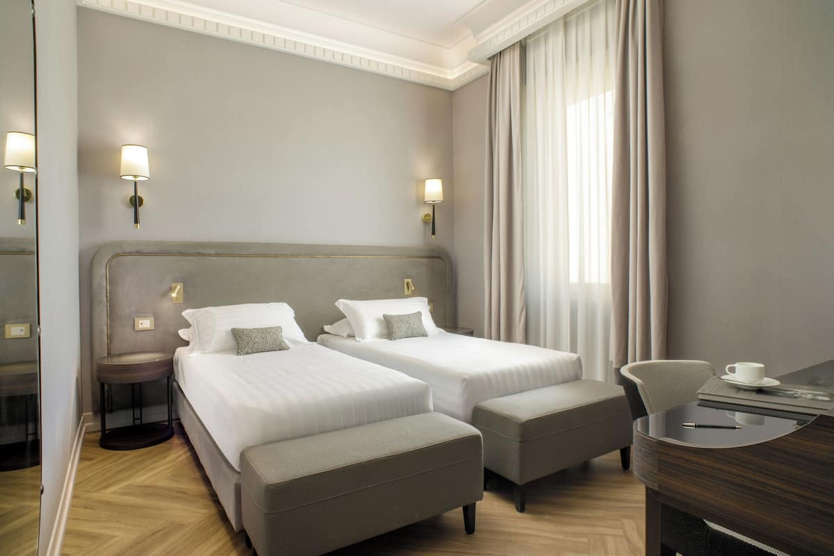 Une chambre d’hôtel avec deux lits, un bureau, une chaise et un miroir.