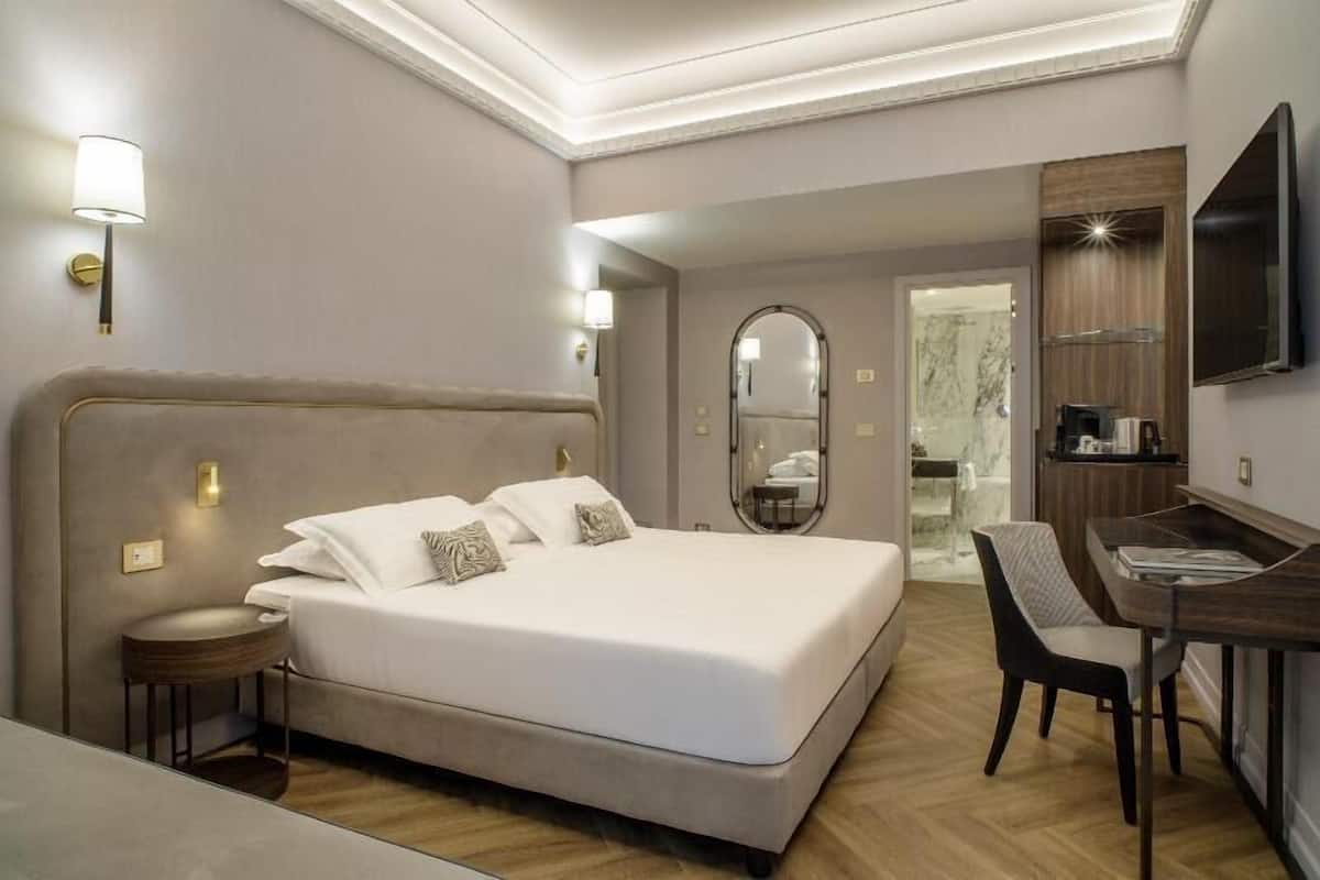 Une chambre d’hôtel comprenant un lit, une table de chevet, une chaise, un bureau et un téléviseur.