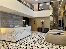 Egy modern előtér márványból készült recepciós pulttal, mintás padlóval és egy kanapéval berendezett ülősarokkal.