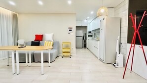 A modern living room with a sofa, a dining table, and a kitchen area with white cabinets and appliances. - 5 mins to Unseo Station, the nearest to the Incheon Airport, Located in Cafe St. (Incheon)