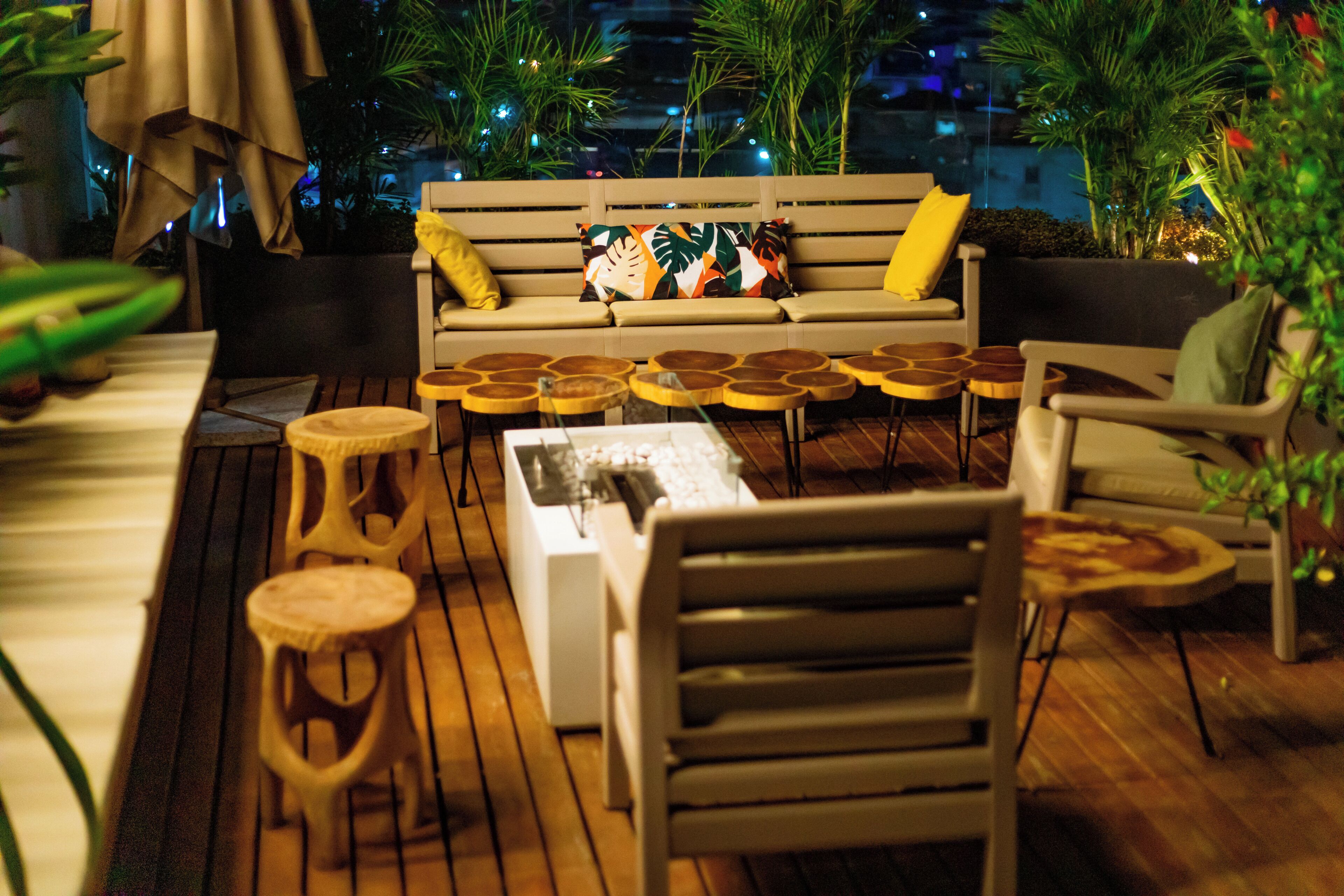 A rooftop terrace with a sofa, round wooden tables, and chairs.