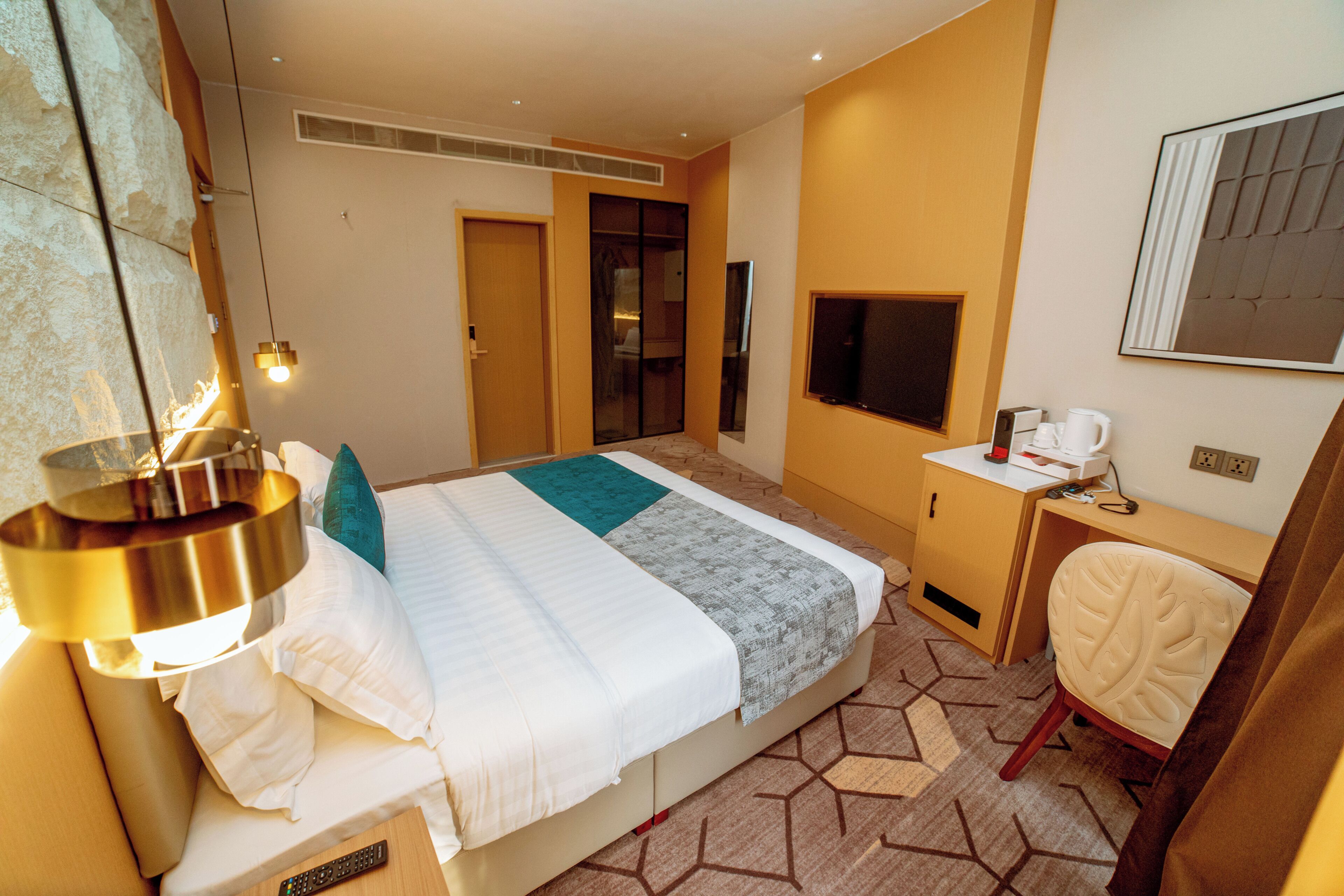 Una habitación de hotel con cama, escritorio, televisor, silla y lámpara.