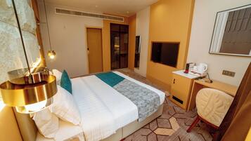 A hotel room with a bed, a desk with a TV, a chair, and a lamp.