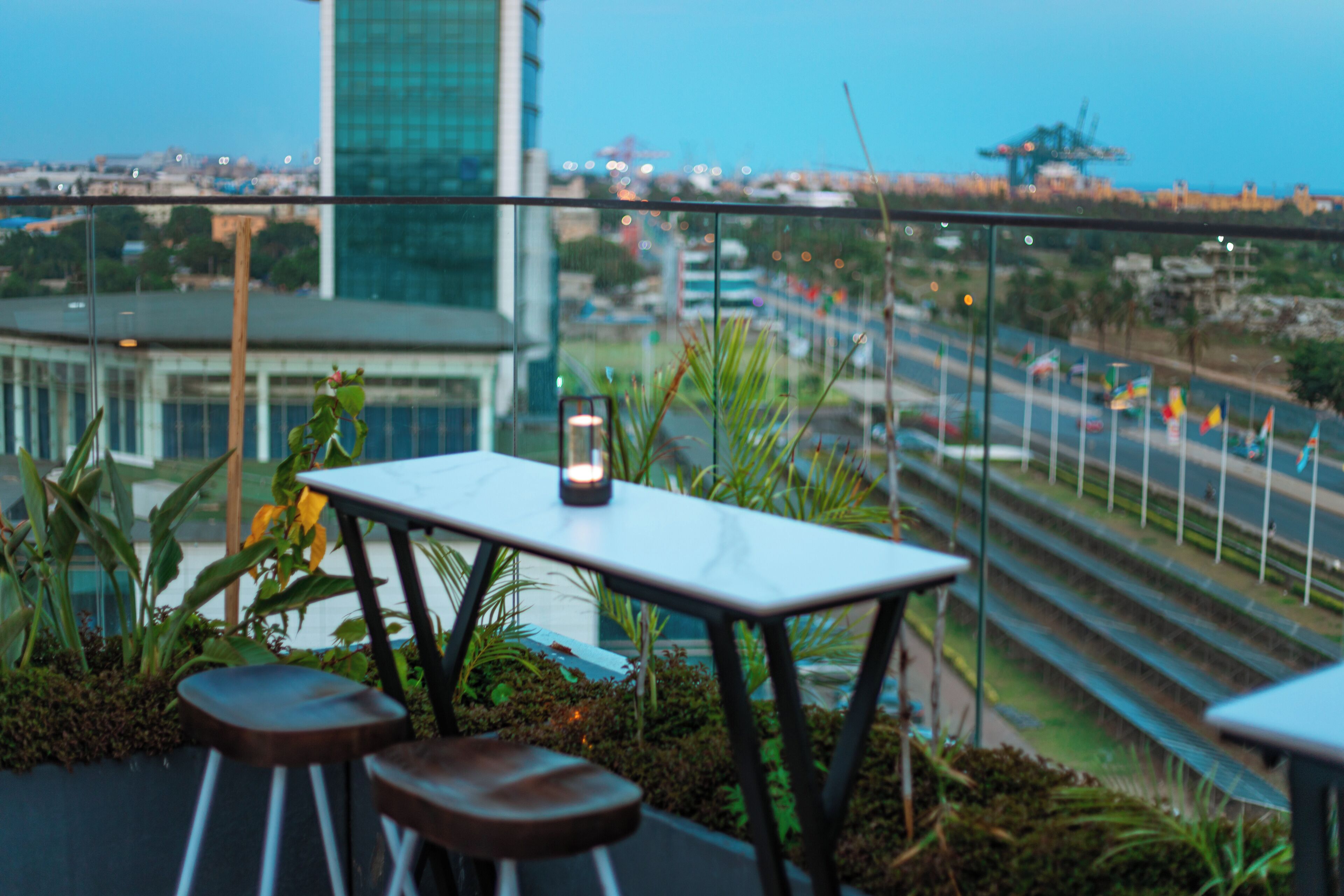 Terraço com mesa e dois banquinhos, com vista para um horizonte urbano com edifícios e uma estrada.