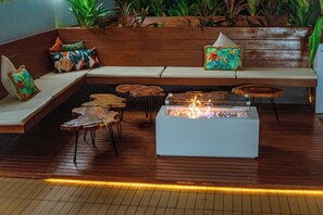 A modern lounge area with a wooden bench, a small fire feature, and a seating area with cushions.