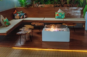 Un área de estar moderna con un banco de madera, un elemento decorativo con fuego y un rincón de asientos con cojines.