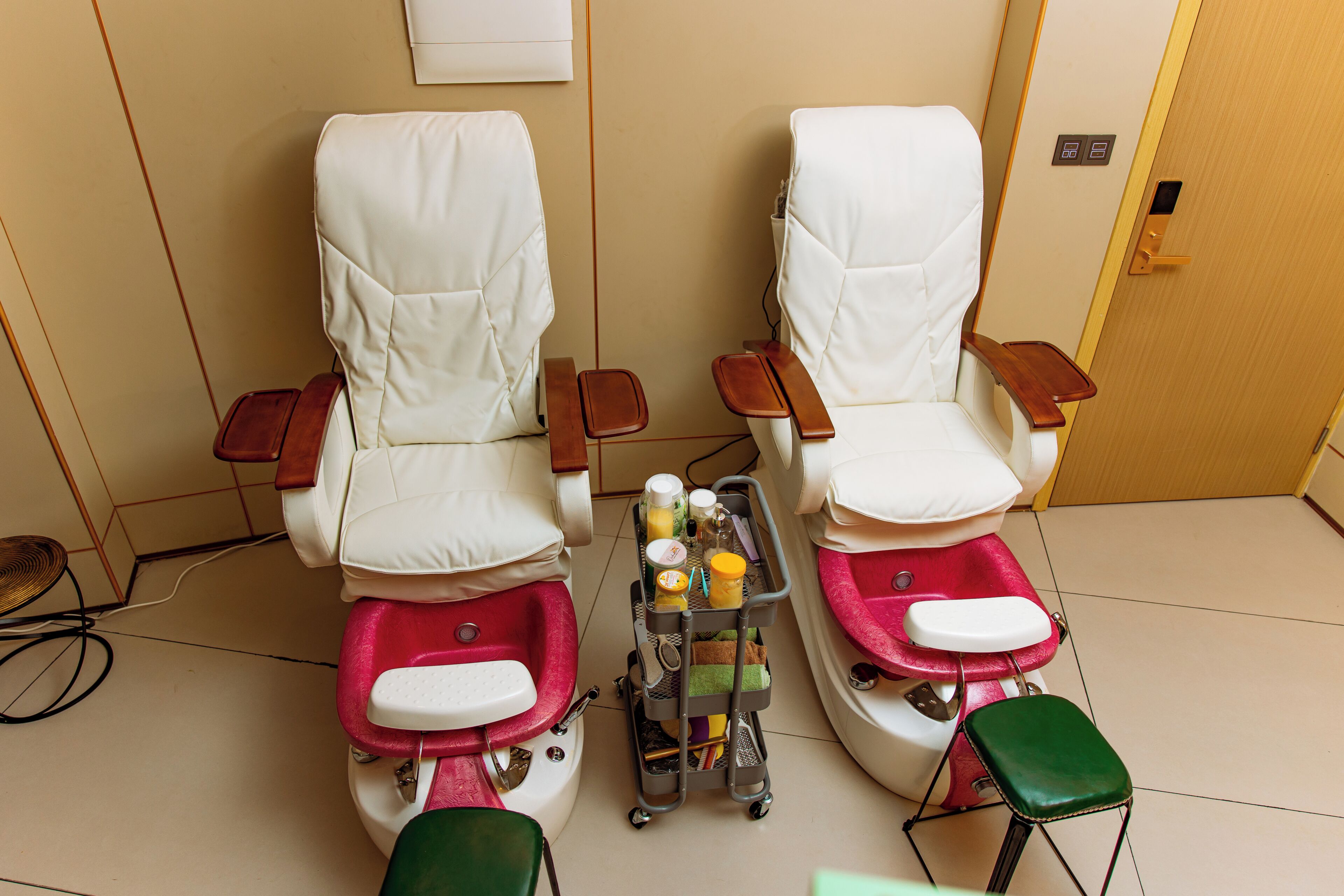 A room with two foot spa chairs, a small table with bottles, and a door with a light switch.
