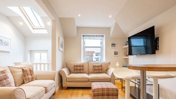 A modern living room with a sofa, ottoman, and a dining table. - Rocklands (No 11) | Elie (Elie)