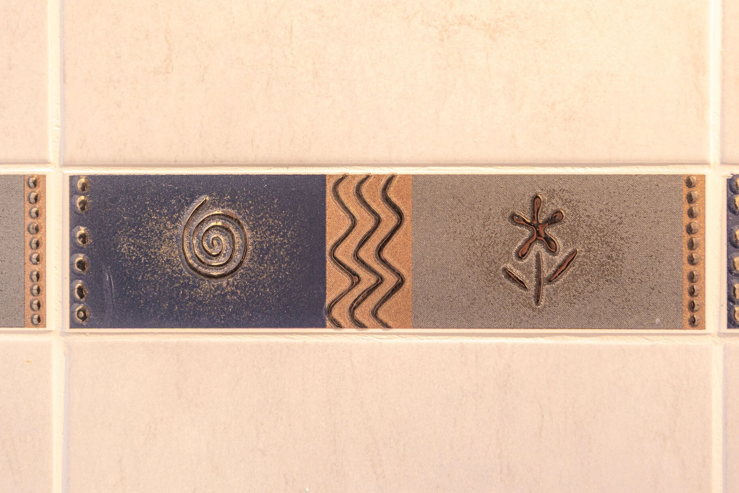 Un mur recouvert de carreaux présentant des motifs décoratifs, notamment des spirales, des motifs en zigzag et des ancres.