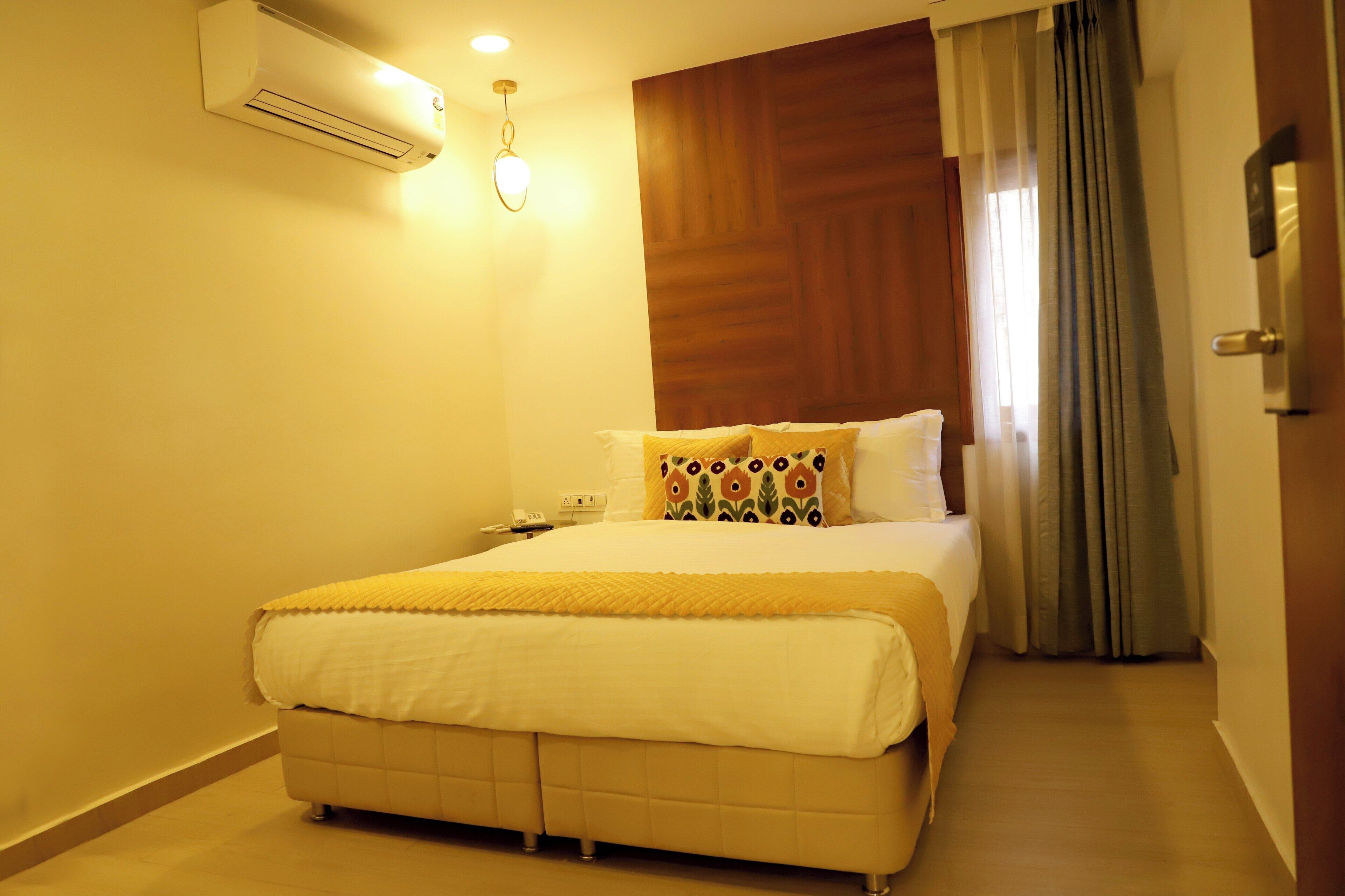 Une chambre d’hôtel avec un lit, un appareil de climatisation, une table de chevet et un rideau.