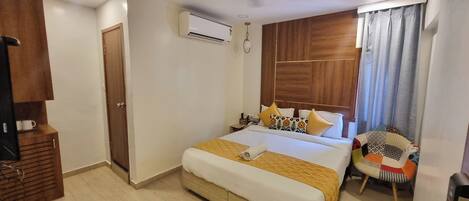 A hotel room with a large bed, wooden headboard, a small desk, and a chair.