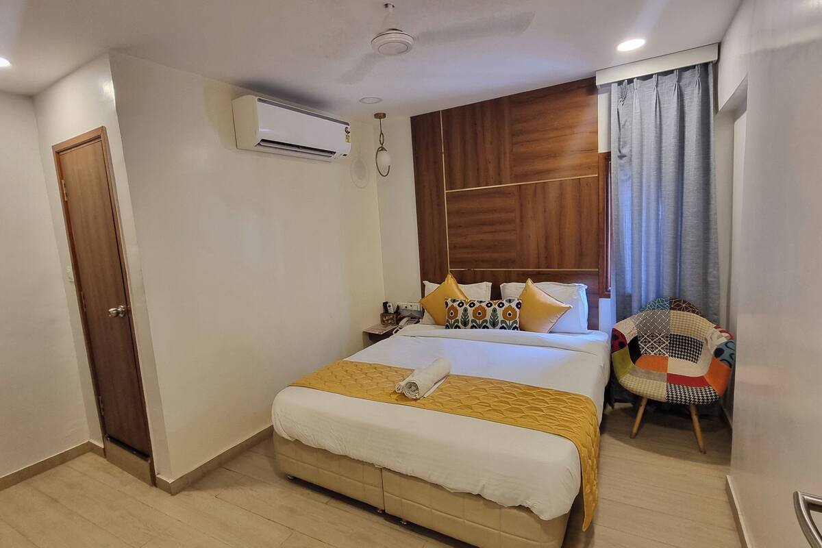A hotel room with a bed, a wooden headboard, a small table, and a chair.