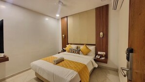 A hotel room with a bed, bedside tables, a wall-mounted TV, and a door with a handle. - Hotel Hinduja Empire (Surat)
