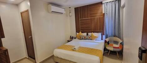 A hotel room with a bed, a chair, an air conditioning unit, and a door.