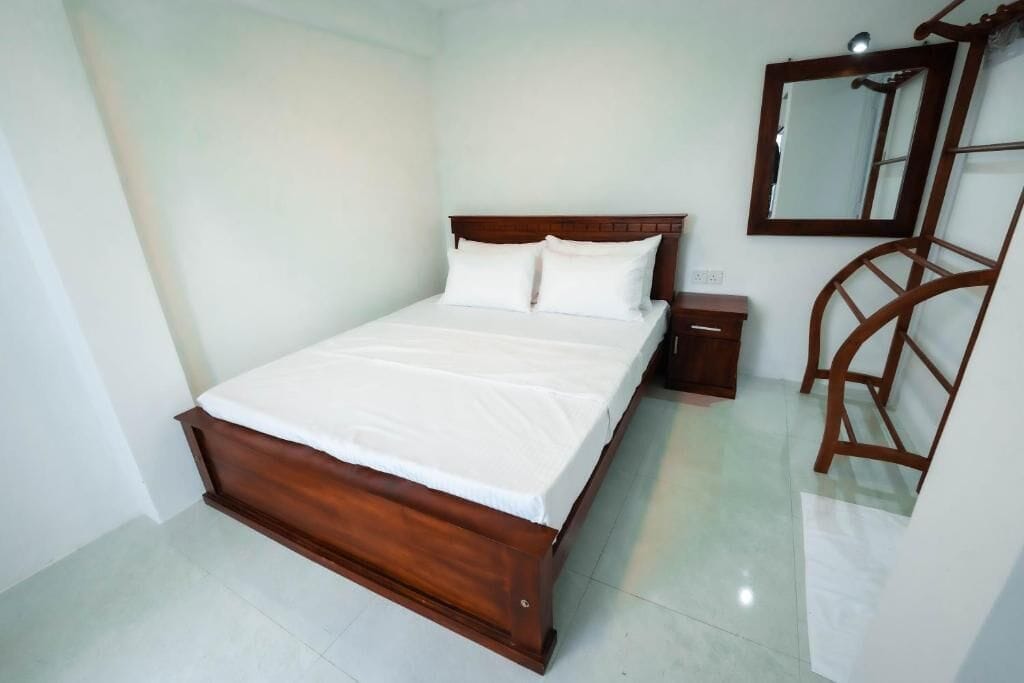 A neatly made bed with a wooden headboard, a bedside table, and a mirror on the wall.