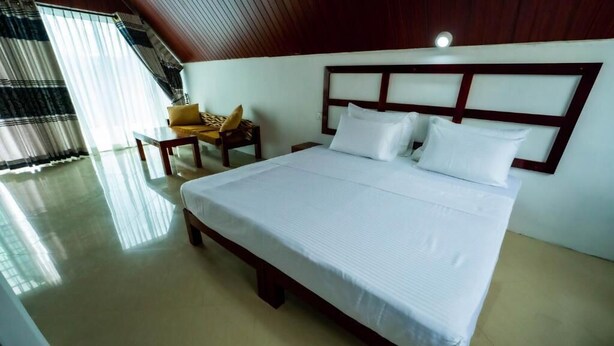 Habitación de hotel con una cama grande, cabecera de madera, una mesita con una silla y una ventana con cortinas.