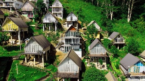 A cluster of houses with multiple stories, some with balconies, situated on a hillside with lush greenery.