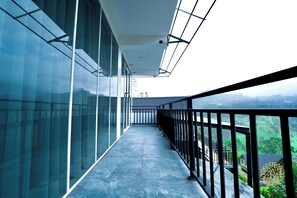 A long, narrow corridor with glass walls on one side and a metal railing on the other, leading to a view of a green landscape.