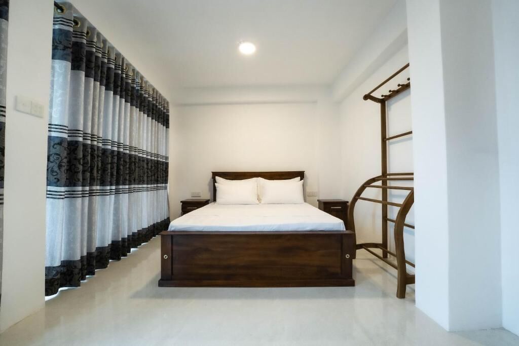 Une chambre avec un lit en bois, du linge de lit blanc, un rideau à motifs sombres et une échelle en bois appuyée contre le mur.